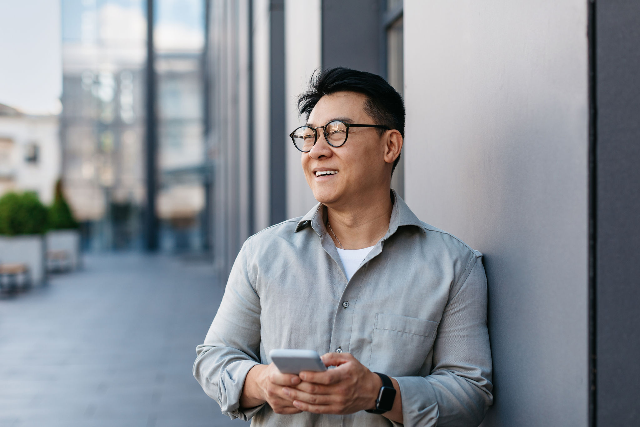 Man standing outdoors, holding a smartphone and looking off into the distance