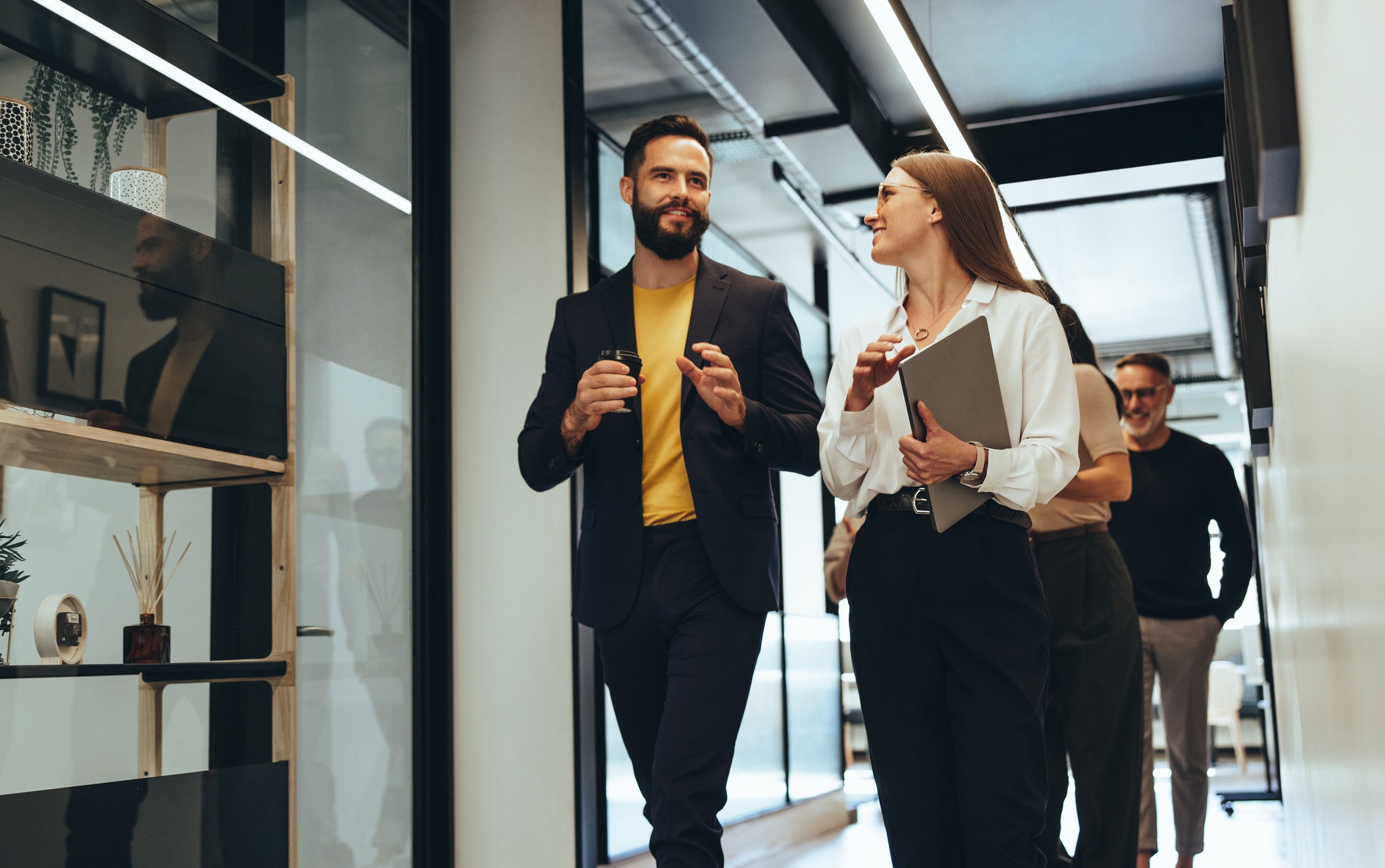 Young professionals having a discussion in a modern office. Two happy young businesspeople smiling while walking together in a hallway. Cheerful colleagues collaborating on a new project.