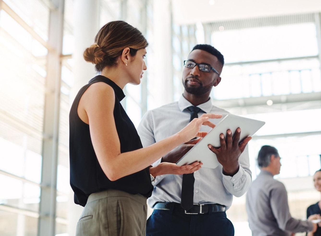 Male and female colleagues standing in an open workspace, discussing a project