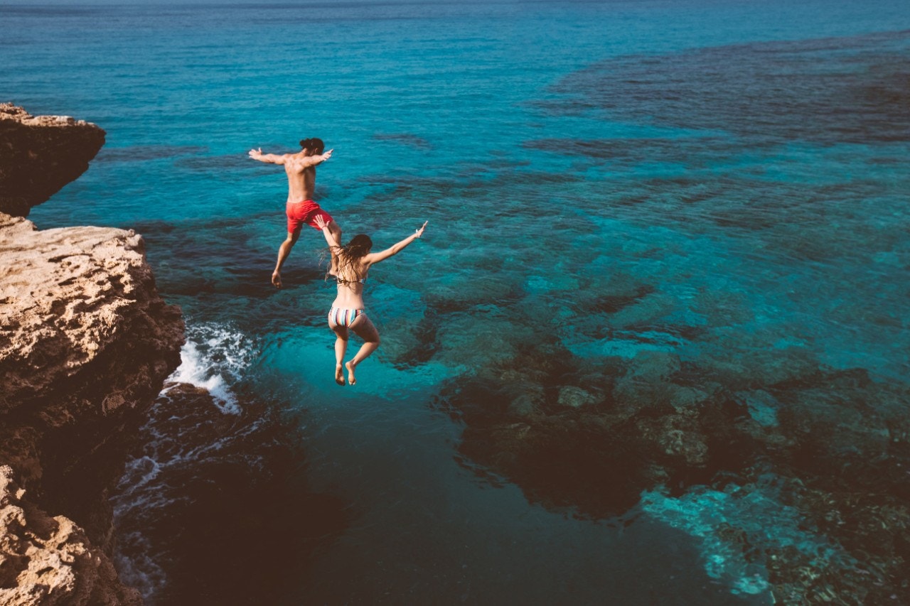 Couple on holiday jumping off cliff into the sea 