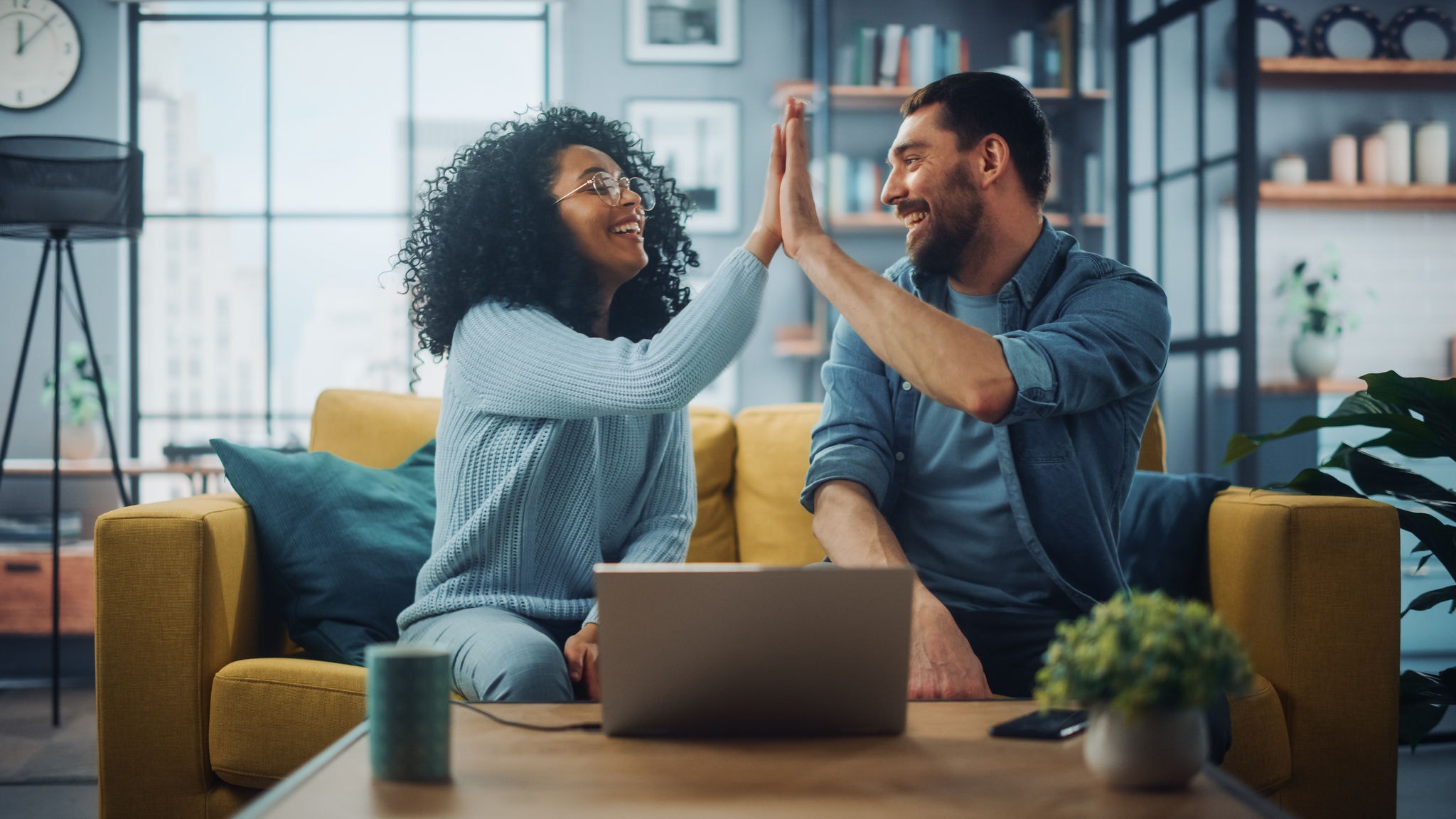 Friends sitting on a couch, high-fiving in front of a laptop