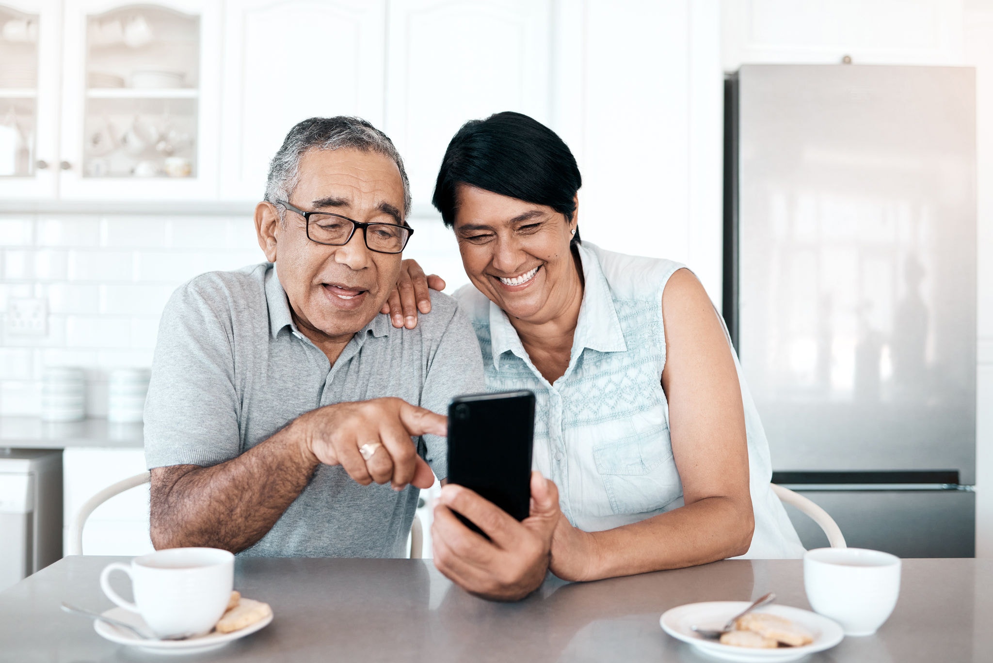 Happy retired couple uses their smartphone at home to FaceTime with loved ones, sharing joyful moments