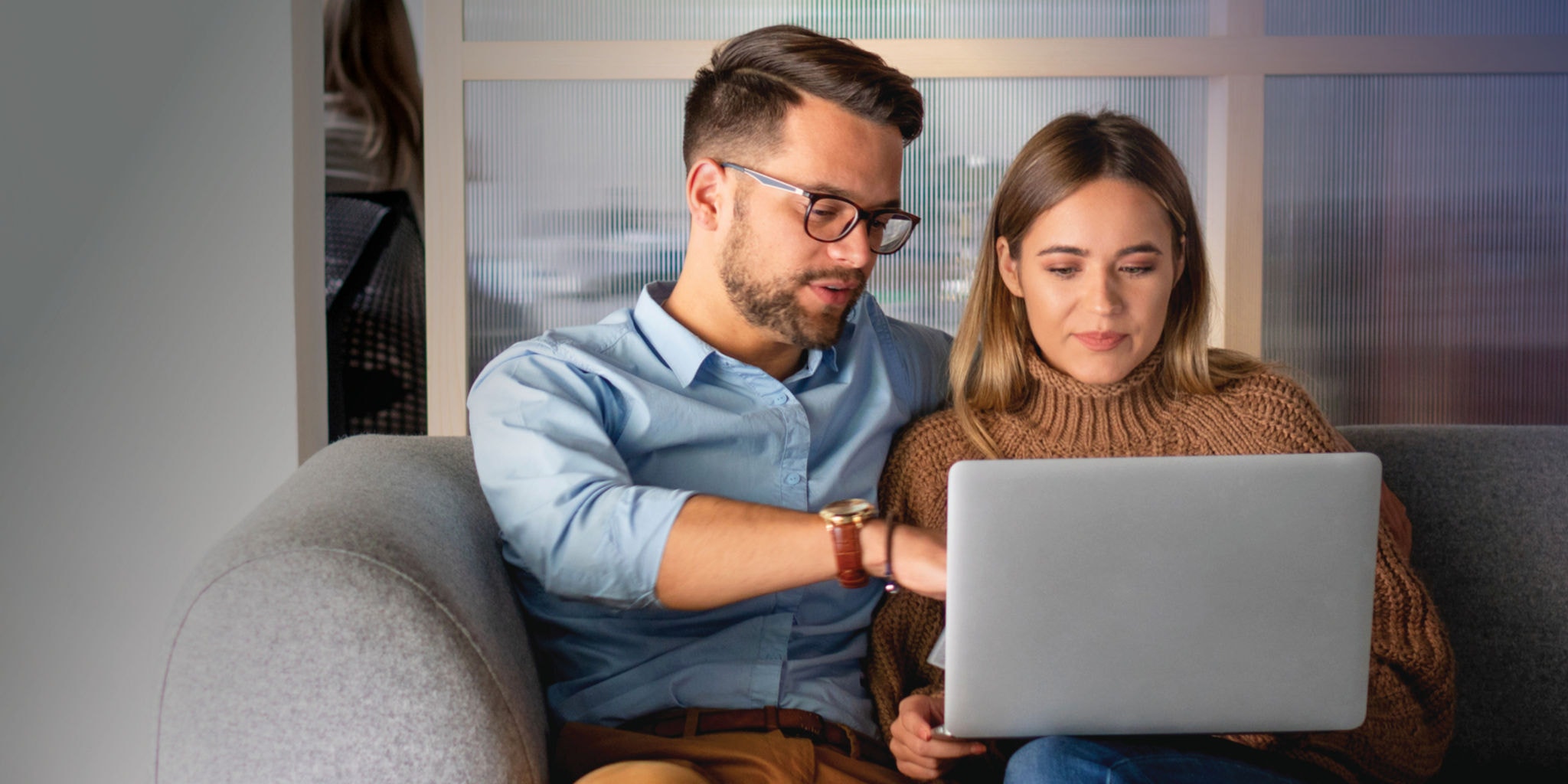Couple sitting on a couch, looking at a laptop