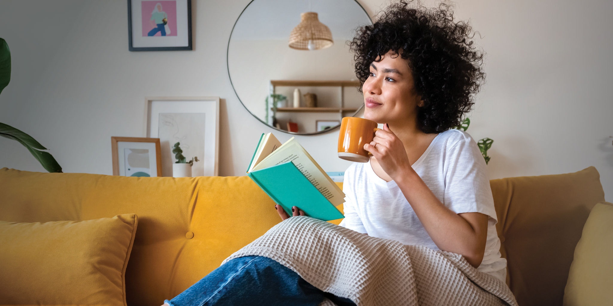 Woman drinking coffee and reading a book looking off into the distance
