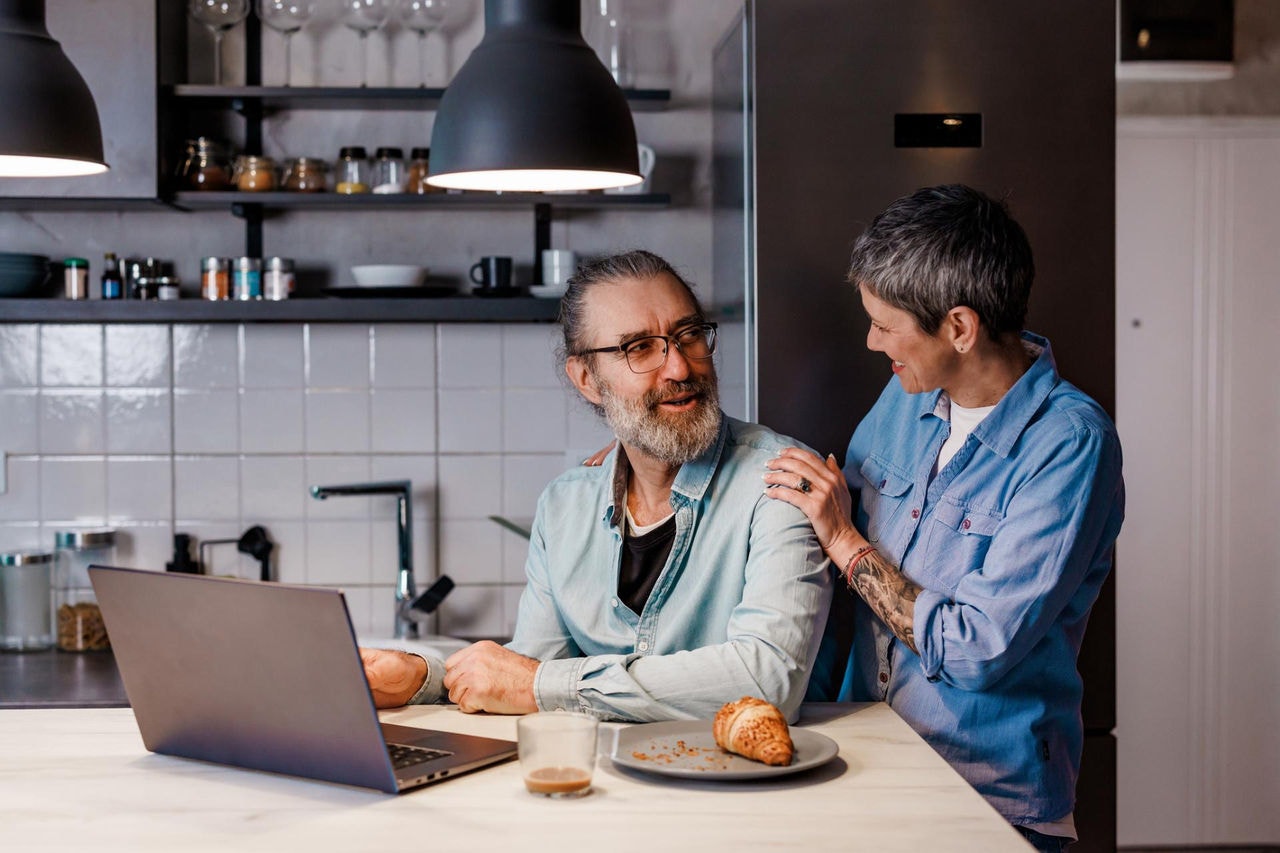 Smiling couple in kitchen using laptop together