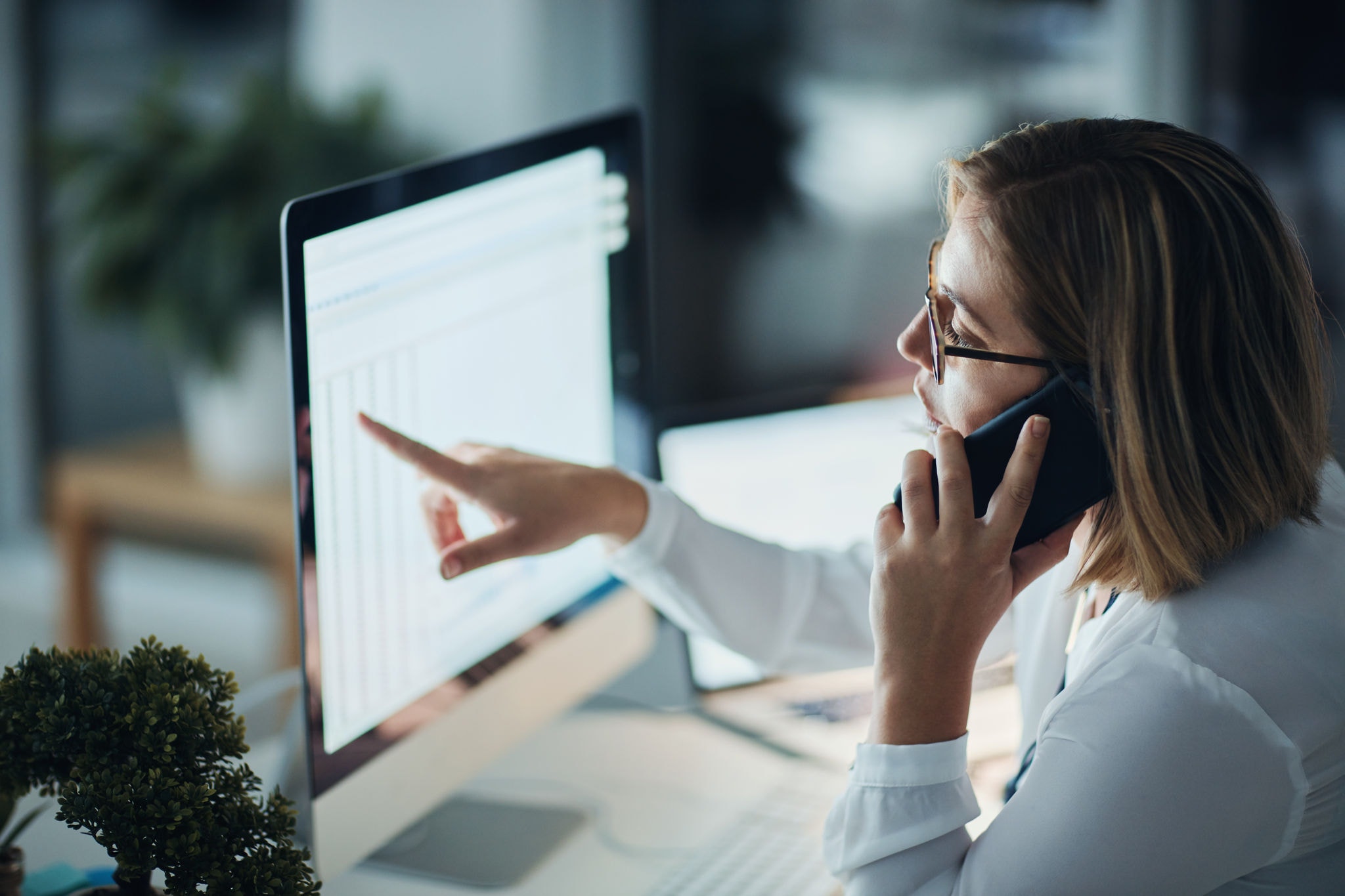 Shot of a businesswoman using a computer and talking on the phone during a late night at work.