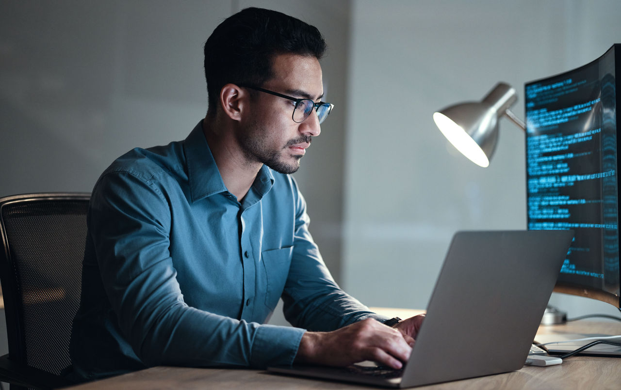 Man coding on a laptop at night, working on cybersecurity and software development